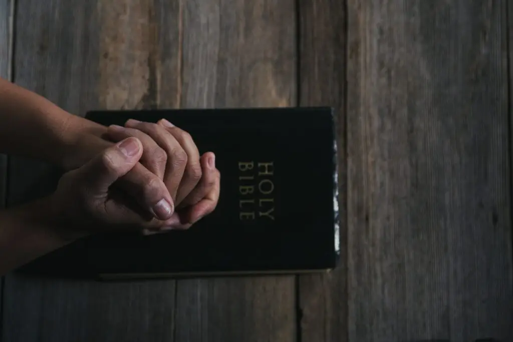 Person praying with a bible on the table